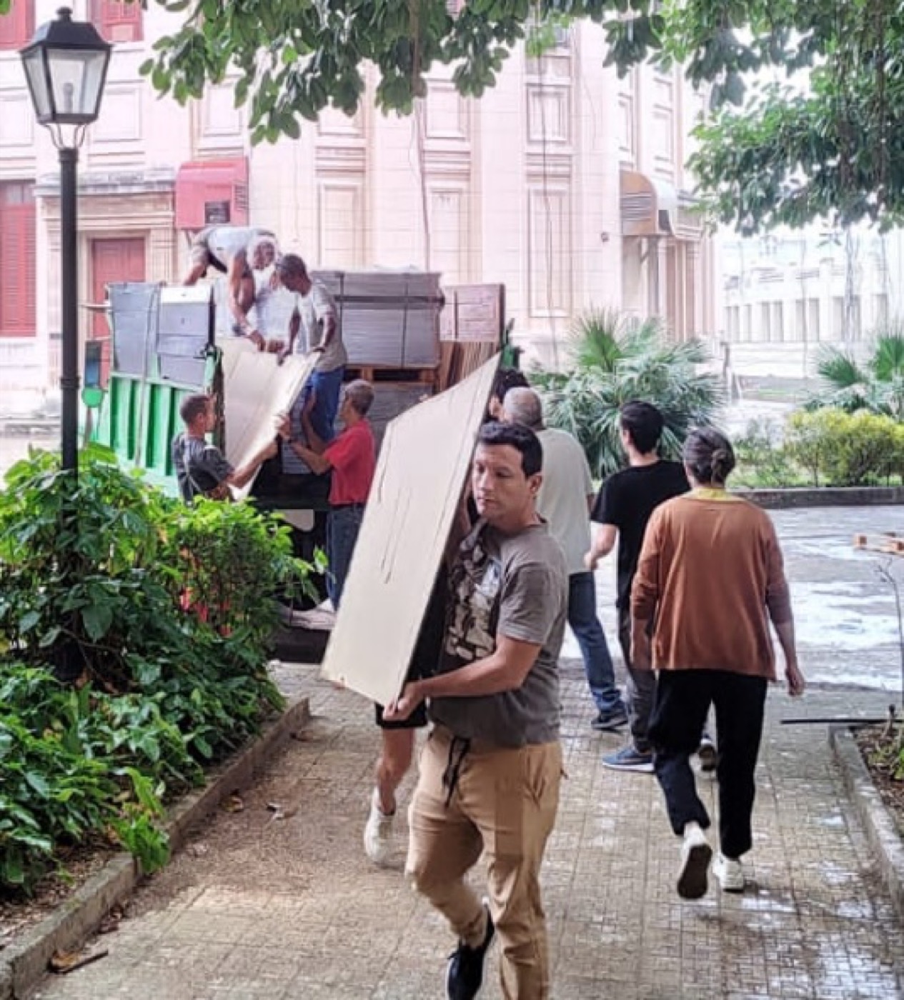 Profesores y estudiantes descargando manualmente planchas de acrílico de un camión.