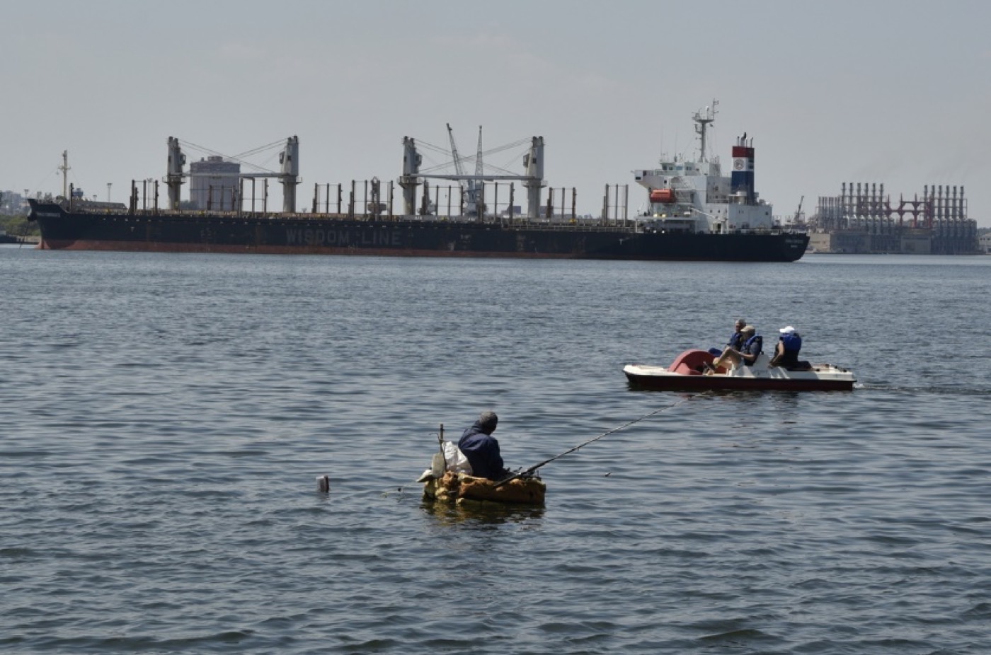 Pescador en una balsa artesanal en la bahía de La Habana, con un carguero de fondo, marzo de 2025.